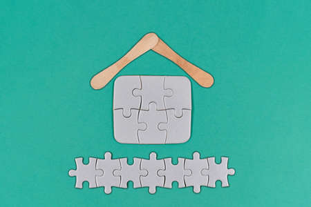 Figure of a house and a fence made of puzzle pieces on a blue paper backgroundの写真素材