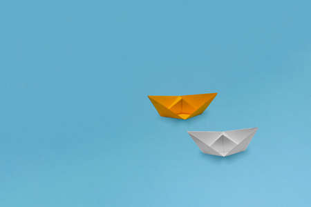 One yellow and one white paper ships (boats) of grainy paper on a blue backgroundの写真素材