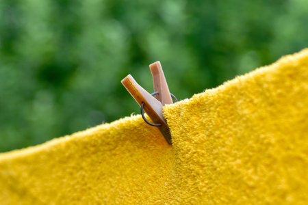 Yellow towel hanging on a rope and attached with a clothespin in the backyardの写真素材