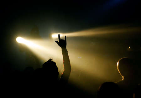 music fan showing devil's sign, yellow light in the backgroundの写真素材