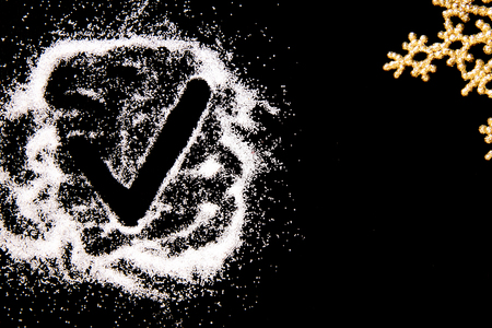 Checking mark symbol drawing by finger on white salt powder spot cloud on left side on black background. Golden snowflake in corner. New year and Christamas tick concept with place for text Copy spaceの写真素材