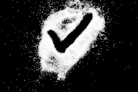 Checking mark symbol drawing by finger on white snow salt powder spot cloud in center on black background. Tick concept with place for text. Copy space.の写真素材
