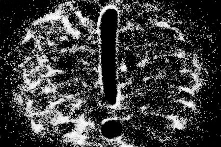 Exclamation mark sign symbol drawing by finger on white snow salt powder on black background. Tick...