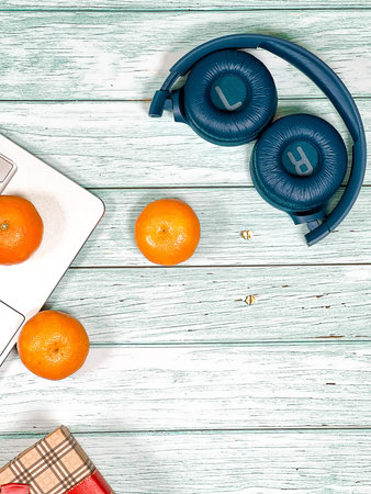 Laptop, headphones and tangerines with a gift box on a vintage board background. A holiday card.
