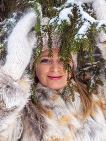 The girl looks through the Christmas tree branches and smiles. The concept of a winter walk.の写真素材