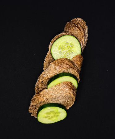 Sliced black bread with fresh vegetables on a dark background. The concept of healthy eating.