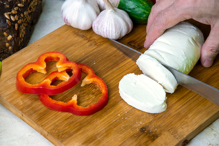 Men's hands cut mozzarella cheese for Greek salad on a cutting board. The concept of healthy eating.の写真素材