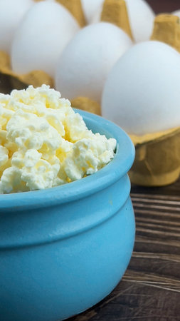 Fresh crumbly cottage cheese close-up on a dark table against the background of white eggs in a tray. homemade food.の写真素材