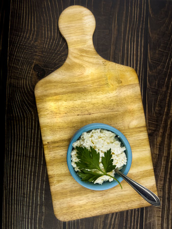 A blue cup with homemade cottage cheese on a kitchen board and a dark table made of boards. The concept of home-made healthy food.の写真素材