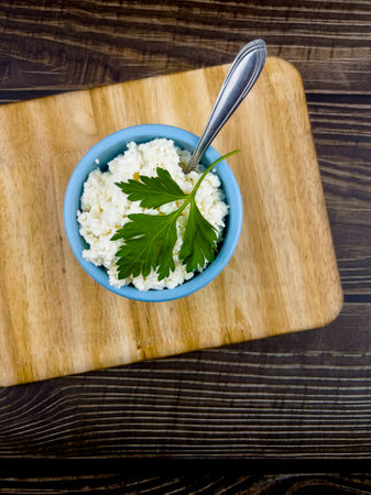 A blue cup with homemade cottage cheese on a kitchen board and a dark table made of boards. The concept of home-made healthy food.の写真素材