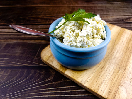A blue cup with homemade cottage cheese on a kitchen board and a dark table made of boards. The concept of home-made healthy food.の写真素材