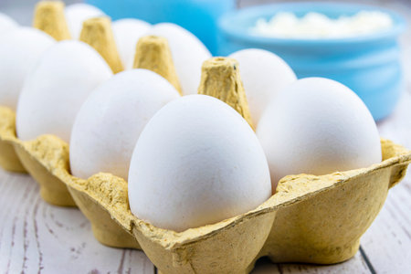 Fresh chicken eggs in a tray on a wooden table against the background of rustic cottage cheese. The...