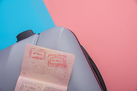 A flat with a gray tourist suitcase, a smartphone, and glasses on a pink-blue background. The concept of travel.の写真素材