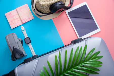 A flat with a gray tourist suitcase, a smartphone, glasses and a drone with a passport on a pink-blue background. The concept of travel.の写真素材