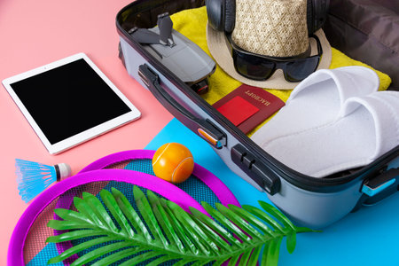 A flat with a gray tourist suitcase, a smartphone, glasses and a passport on a pink-blue background....