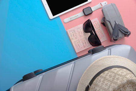 A flat with a gray tourist suitcase, a smartphone, and glasses on a pink-blue background. The concept of travel.の写真素材