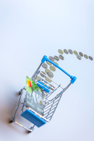 A supermarket cart on a white background with a trail of coins and a credit card. The concept of online shopping.の写真素材