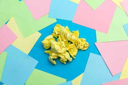 A bunch of yellow crumpled yellow pieces of paper on a blue background among colorful pieces of paper. The concept of finding an idea. Close-up.の写真素材