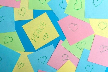 A yellow piece of paper with the inscription PEACE on a blue background among colorful pieces of paper. The concept of peace on earth with different opinions. Close-up.の写真素材