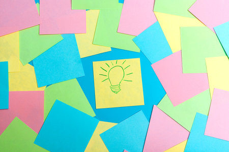 Yellow notepaper with a painted burning lamp lies on a blue background between colored pieces of...