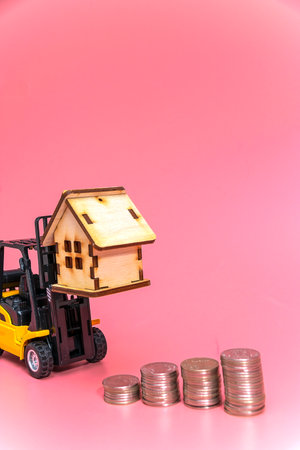 A forklift truck holds a model of a house on a pink background on a platform. The concept of buying real estate. Copy space.の写真素材