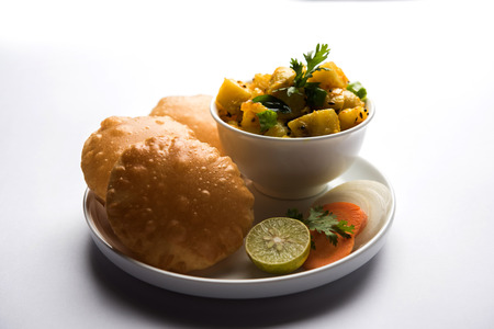 Chatpate Masala Aloo Sabzi fry OR Bombay potatoes served with fried puri or Indian bread made up of wheat in a plate, selective focusの写真素材