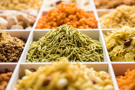 Indian Tea-time snacks like sev, chivda, farsan, mixture, boondi, bakarwadi etc served in white wooden box with cells. selective focusの写真素材