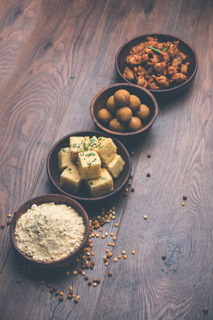 Chick pea flour or Besan powder in a ceramic or wooden bowl along with Gujrati Dhokla snack, onion bajji or bhaji and sweet laddu or laddooの写真素材