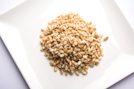 Raw and cooked Barley pearl seeds in a bowl or over white plate. selective focusの写真素材