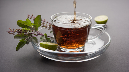 pouring Holy Basil or Tulsi Tea in transparent glass cup with saucer over white or black background. Popular Ayurvedic medicine from Indiaの写真素材
