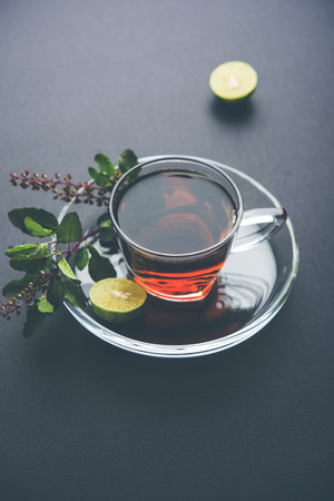 pouring Holy Basil or Tulsi Tea in transparent glass cup with saucer over white or black background. Popular Ayurvedic medicine from Indiaの写真素材