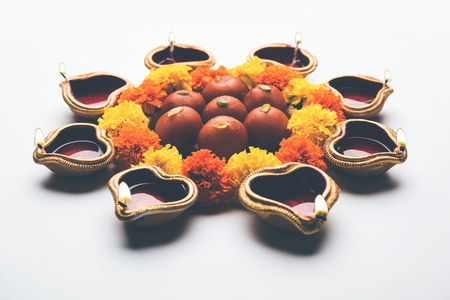 Diwali Rangoli using Diya/oil lamp, flowers and Gulab Jamun arranged over white background, selective focusの写真素材