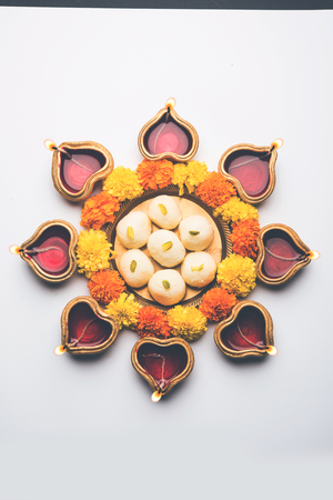 Diwali Rangoli using Diya/oil lamp, flowers and Rasgulla/rosogulla arranged over white background, selective focusの写真素材