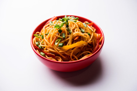 Schezwan Noodles or vegetable Hakka Noodles or chow mein is a popular Indo-Chinese recipes, served in a bowl or plate with wooden chopsticks. selective focusの写真素材