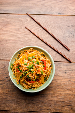 Schezwan Noodles or vegetable Hakka Noodles or chow mein is a popular Indo-Chinese recipes, served in a bowl or plate with wooden chopsticks. selective focusの写真素材