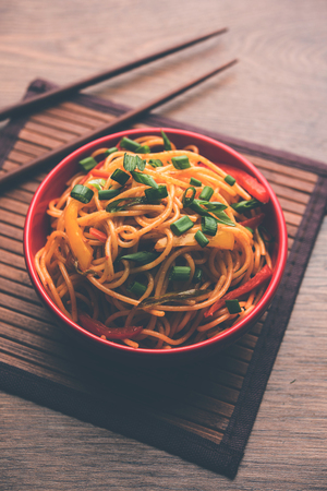 Schezwan Noodles or vegetable Hakka Noodles or chow mein is a popular Indo-Chinese recipes, served in a bowl or plate with wooden chopsticks. selective focusの写真素材