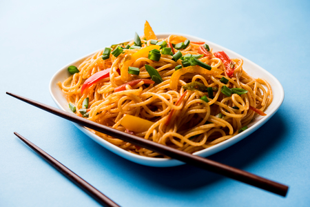 Schezwan Noodles or vegetable Hakka Noodles or chow mein is a popular Indo-Chinese recipes, served in a bowl or plate with wooden chopsticks. selective focusの写真素材