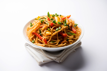 Schezwan Noodles or vegetable Hakka Noodles or chow mein is a popular Indo-Chinese recipes, served in a bowl or plate with wooden chopsticks. selective focusの写真素材