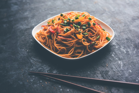 Schezwan Noodles or vegetable Hakka Noodles or chow mein is a popular Indo-Chinese recipes, served in a bowl or plate with wooden chopsticks. selective focusの写真素材