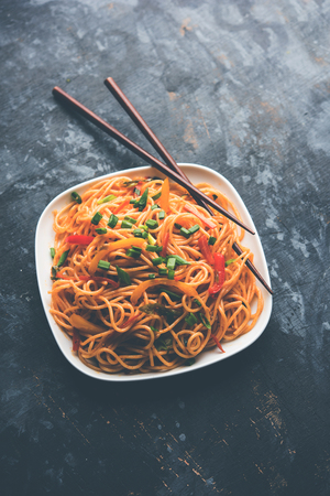 Schezwan Noodles or vegetable Hakka Noodles or chow mein is a popular Indo-Chinese recipes, served in a bowl or plate with wooden chopsticks. selective focusの写真素材