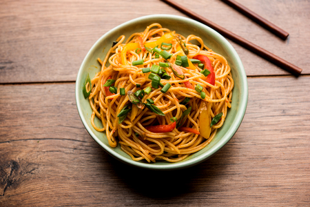 Schezwan Noodles or vegetable Hakka Noodles or chow mein is a popular Indo-Chinese recipes, served in a bowl or plate with wooden chopsticks. selective focusの写真素材