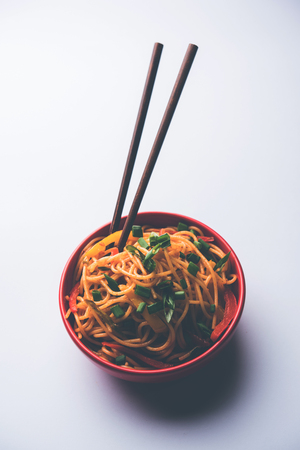 Schezwan Noodles or vegetable Hakka Noodles or chow mein is a popular Indo-Chinese recipes, served in a bowl or plate with wooden chopsticks. selective focusの写真素材