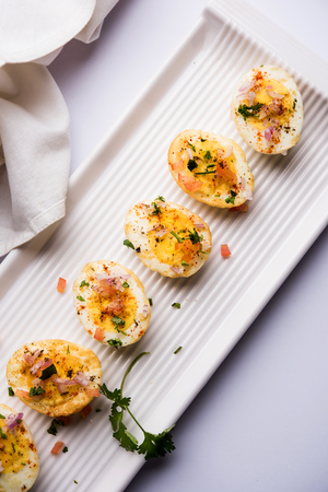 Fried hot boiled egg masala is a popular healthy breakfast or starter menu from India. With onion, coriander, black pepper, tomato and salt sprinkled over half of eggsの写真素材