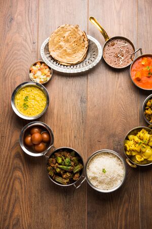 Assorted Indian food like paneer butter masala, dal, roti, rice, sabji, gulab jamun and bound raita served in bowls over moody background, selective focusの写真素材