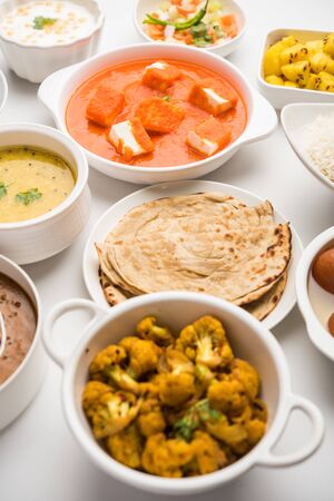 Assorted Indian food like paneer butter masala, dal, roti, rice, sabji, gulab jamun and bound raita served in bowls over moody background, selective focusの写真素材