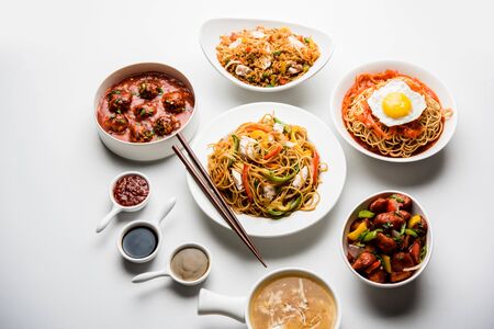 Assorted Indo chinese food in group includes non vegetarian or chicken Schezwan/Szechuan hakka noodles, fried rice, manchurian, egg american chop suey, soup with spoon and chop sticks, selective focusの写真素材