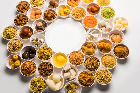 Rangoli of sweets and Farsan/snacks in bowls for Diwali with diya over white backgroundの写真素材
