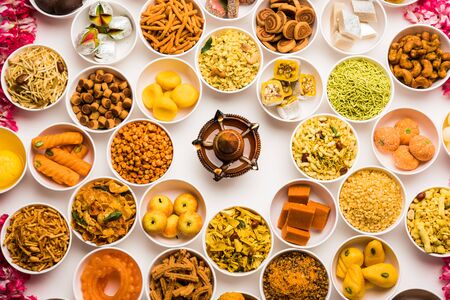 Rangoli of sweets and Farsan/snacks in bowls for Diwali with diya over white backgroundの写真素材