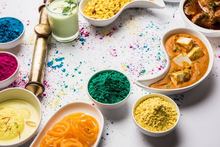 Happy Holy concept  showing Indian assorted lunch food like chicken, paneer butter masala, naan, jeera rice, black chana fry, jalebi, fujiyama, thandai and Farsan with holi colours and pichkariの写真素材
