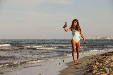 Young girl walking on the beach with mobile phoneの写真素材